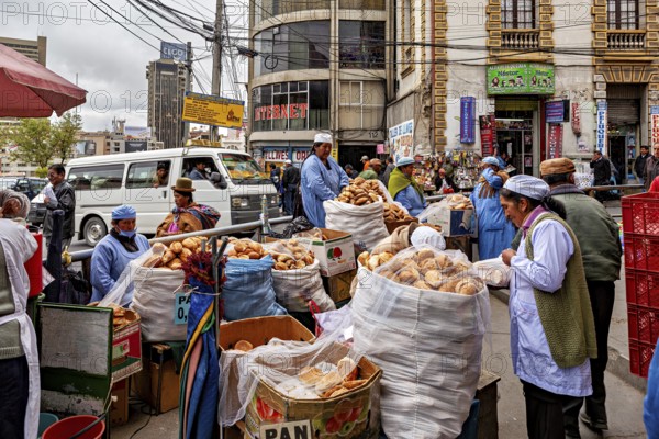 A bustling city market with bread stalls and vendors in a busy street between tall buildings, woman selling in the streets of La Paz, Bolivia