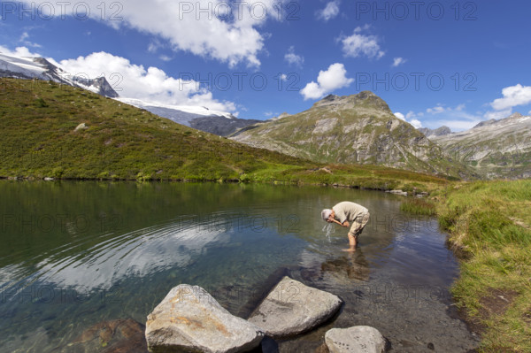 Hiker refreshes himself in the Salzbodensee lake on the glacier show trail in the Tauerntal valley, Hohe Tauern National Park, East Tyrol, Austria