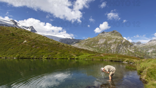 Hiker refreshes himself in the Salzbodensee lake on the glacier show trail in the Tauerntal valley, Hohe Tauern National Park, East Tyrol, Austria