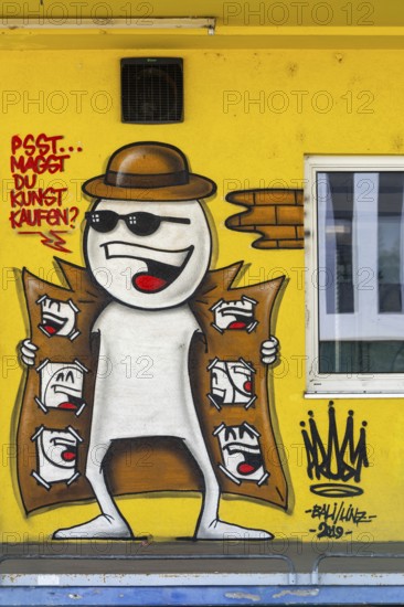 Funny comic-style graffiti with a figure in a trench coat on a yellow wall, at the harbour in Linz, Upper Austria Austria