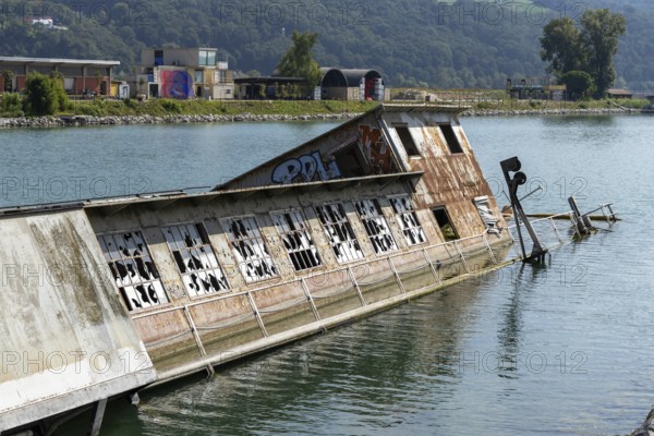 Partially submerged ship with graffiti near shore with mountains, at the harbour Linz Upper Austria Austria