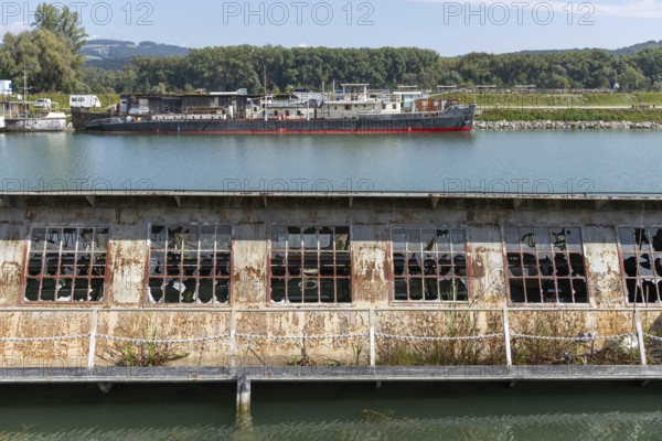 Dilapidated industrial building with destroyed windows directly on the waterfront, at the harbour Linz Upper Austria Austria