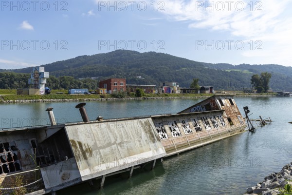 Abandoned capsized ship in the water with mountain in the background, at the harbour Linz Upper Austria Austria