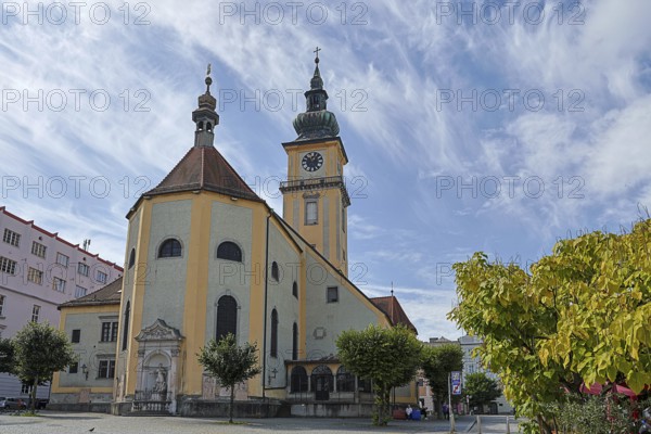 Baroque church with clock tower and trees on a sunny square, blue sky, Stadtpfarrkirche Maria Himmelfahrt Linz Austria
