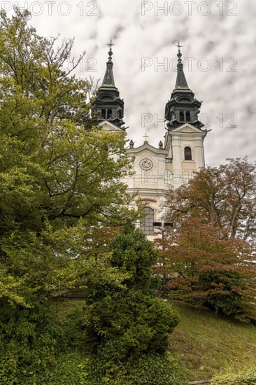 Historic church with two towers behind autumnal trees in front of a cloudy sky, Pöstlingsbergkirche pilgrimage basilica Sieben Schmerzen Maria Linz Upper Austria Austria