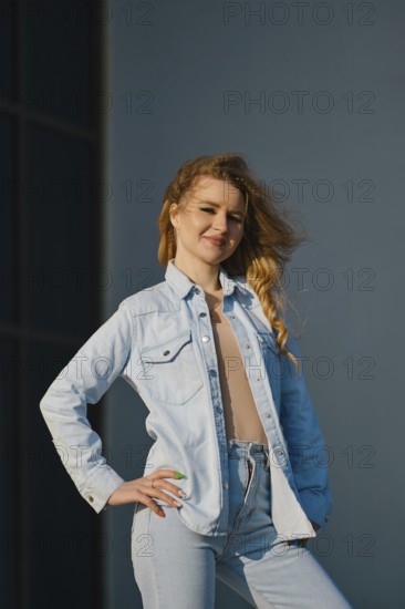 A young woman stands confidently, showcasing a light denim jacket and high-waisted jeans. The sunlight shines on her hair, creating a bright and engaging atmosphere