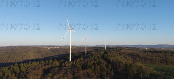 A row of wind turbines towers over a wooded hill under a clear sky, near Schorndorf in the Rems Valley, Baden-Württemberg, Germany
