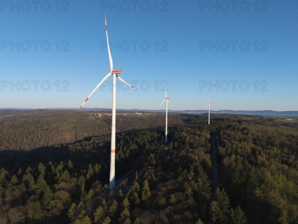 Wind turbines rise above the forest under a cloudless blue sky, near Schorndorf im Remstal, Baden-Württemberg, Germany