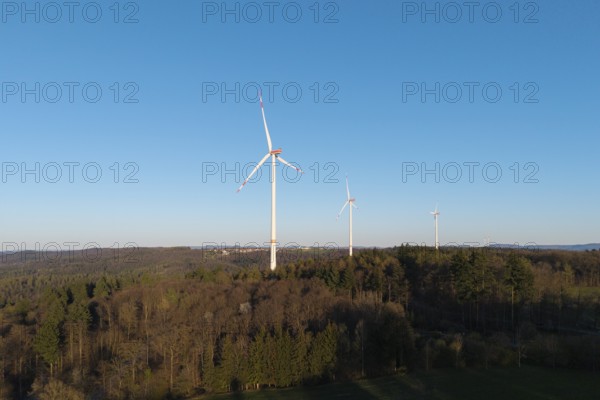 Three wind turbines stand in a wooded landscape under a clear sky, near Schorndorf in the Rems Valley, Baden-Württemberg, Germany