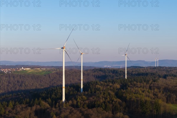 Several wind turbines stretch across a wooded landscape under a clear sky, near Schorndorf in the Rems Valley, Baden-Württemberg, Germany