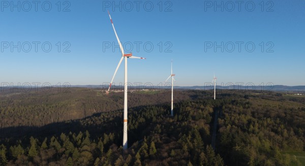 Several wind turbines tower above the treetops of a forest under a blue sky, near Schorndorf in the Rems Valley, Baden-Württemberg, Germany
