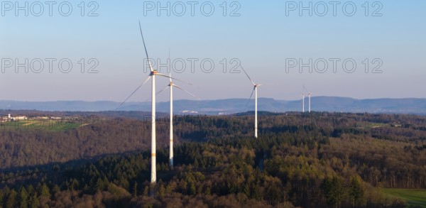 Wind turbines stand on a forest landscape with a clear blue sky in the background, near Schorndorf in the Rems Valley, Baden-Württemberg, Germany