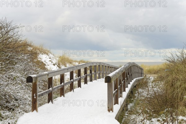Winter day, onset of winter, wooden plank path leads through the snow-covered dune landscape to the North Sea, Norddeich, Lower Saxony, Germany
