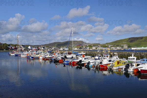 A busy harbour with brightly painted boats in calm waters and a slightly cloudy sky, Scalloway, Shetland Islands, Scotland, United Kingdom