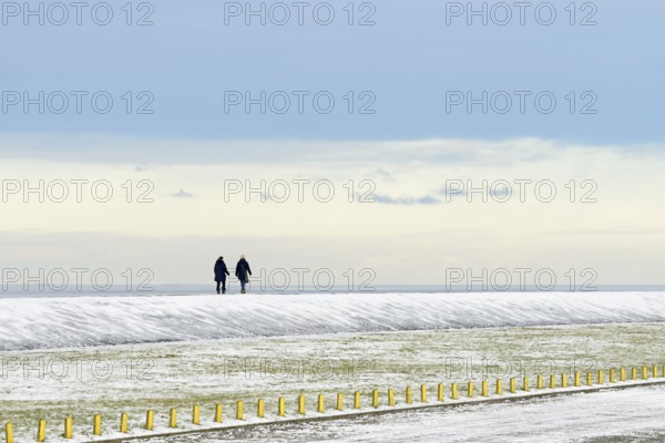 North Sea coast on a winter's day, people walking over a snow-covered dyke, Norddeich, Lower Saxony, Germany