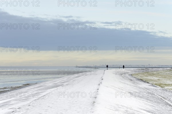 North Sea coast on a winter's day, people walking over a snow-covered dyke, the island of Norderney on the horizon, Norddeich, Lower Saxony, Germany