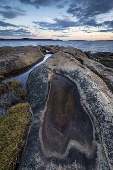 Rocky coastline with water puddles and grass during a sunset-lit evening, Skjeberg, Sarpsborg, Ostfold, Norway