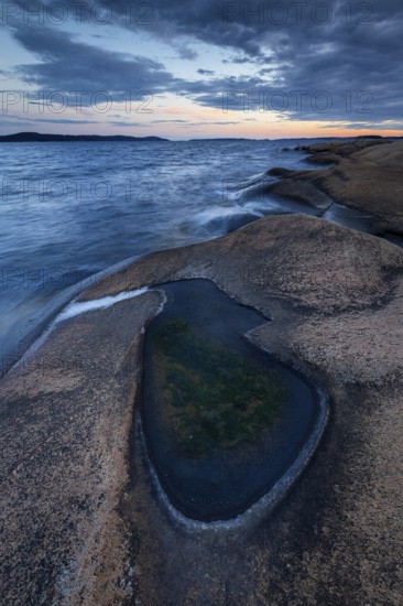 Rocks on the coast with puddle of water while evening light shines through clouds on the horizon, Skjeberg, Sarpsborg, Ostfold, Norway