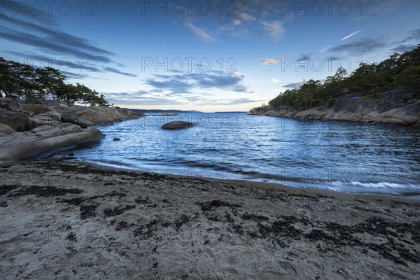 Small bay with sand and rocks, surrounded by pine trees under a partly cloudy sky, Skjeberg, Sarpsborg, Ostfold, Norway