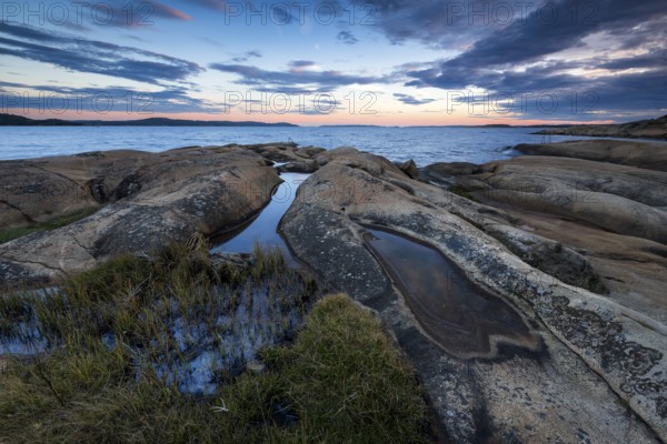 Large rocks with puddles on the coast during a sunset with clouds in the sky, Skjeberg, Sarpsborg, Ostfold, Norway