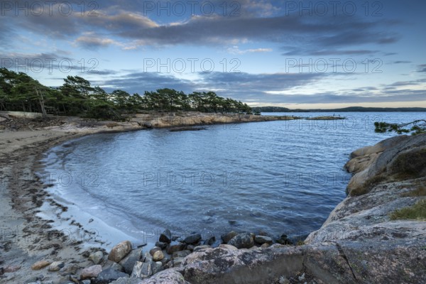 Small bay with sandy beach, surrounded by rocks and pine trees under a partly cloudy sky, Skjeberg, Sarpsborg, Ostfold, Norway