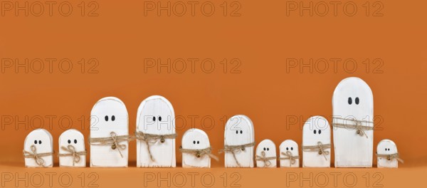 Banner with cute wooden white Halloween ghost ornaments in a row on orange background