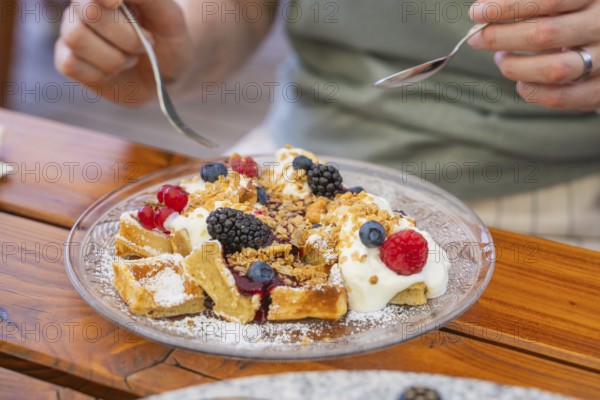 Person enjoying waffles with cream and berries on a wooden table
