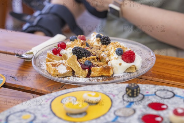 Waffles with cream and berries on a plate, close-up on a wooden table