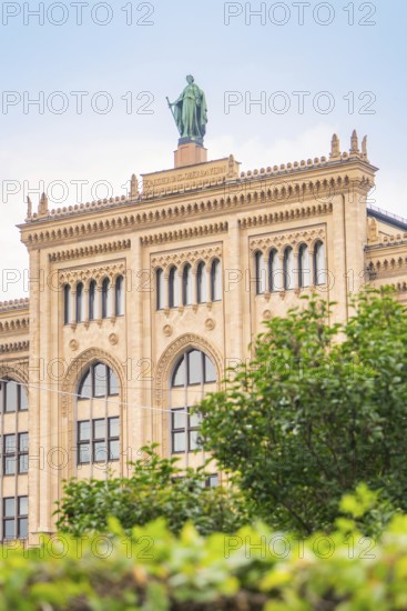 Large historic building with statue on the roof, surrounded by green vegetation, Munich, Germany