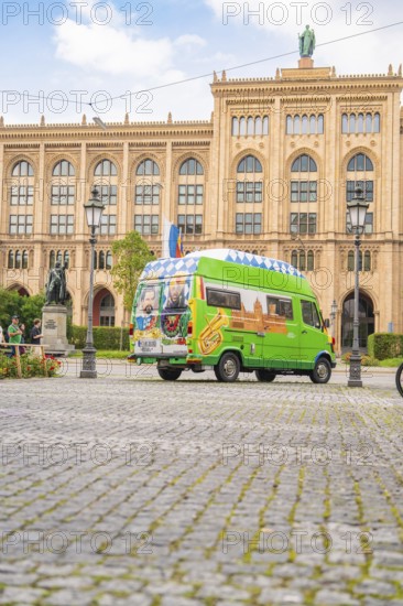A colourfully painted bus in front of a historic building with a cobbled street and lanterns, Munich, Germany