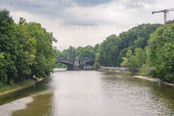 River view with a stone bridge in the background, surrounded by dense forests and a peaceful atmosphere, Munich, Germany