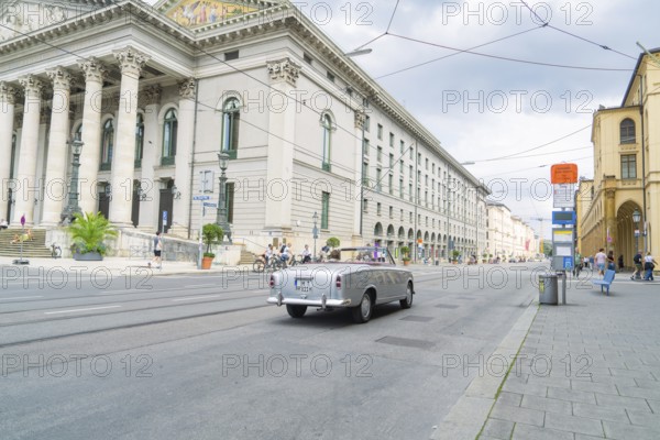 A classic car drives alongside a magnificent building in Munich, Munich, Germany