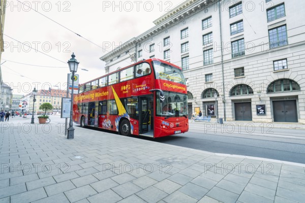 Red double-decker bus on a city street with historic buildings, Munich, Germany