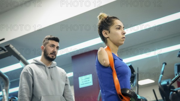 A young female athlete with limb loss trains in a fitness gym with the support of her coach, focusing on strength and rehabilitation exercises, Gaziantep, Gaziantep, Türkiye
