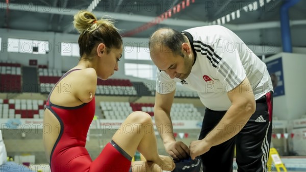 A coach assists a female swimmer with limb loss in adjusting her swim cap before training in an indoor swimming pool, Gaziantep, Gaziantep, Türkiye