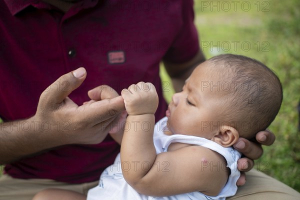 Thoughtful baby interacts with a man's fingers indoors-Dhaka, Bangladesh