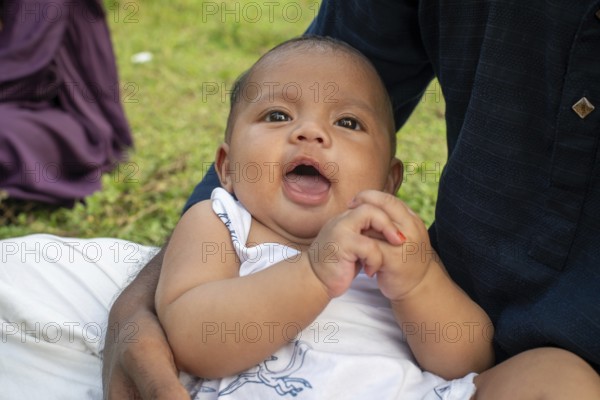 Baby sits with an open mouth, appearing curious outdoors-Dhaka, Bangladesh