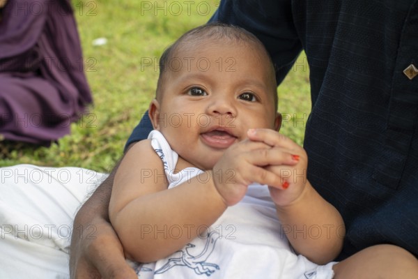 Baby sits on the ground, looking curious in an outdoor setting-Dhaka, Bangladesh