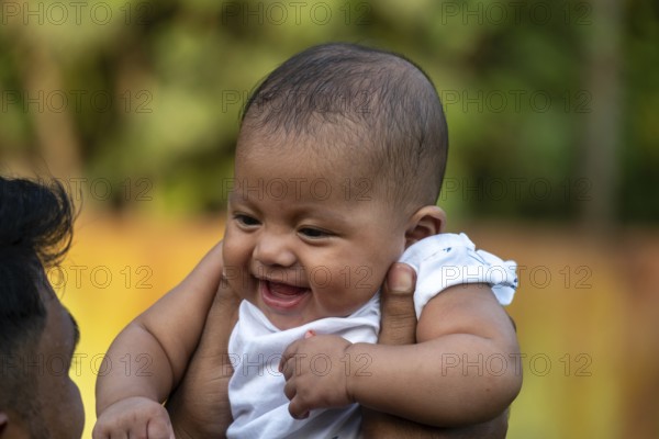 Cheerful baby smiles in delight while lifted outdoors-Dhaka, Bangladesh