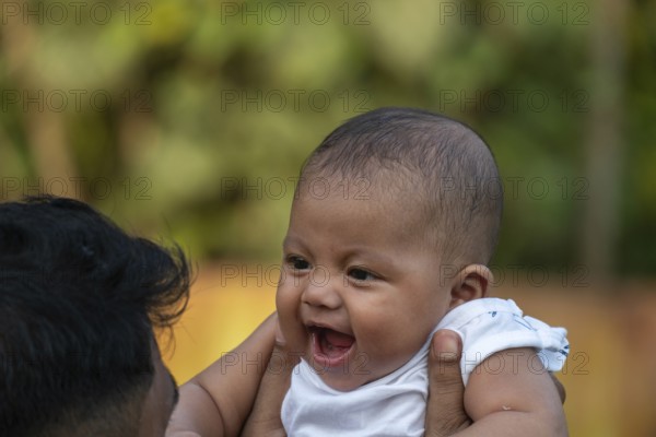 Baby smiles happily while being held up outdoors-Dhaka, Bangladesh
