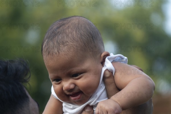 Baby being lifted up and smiling joyfully outdoors