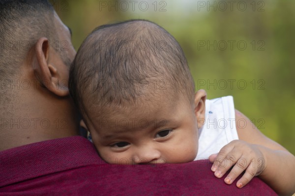 Baby rests peacefully on a man's shoulder outdoors-Dhaka, Bangladesh