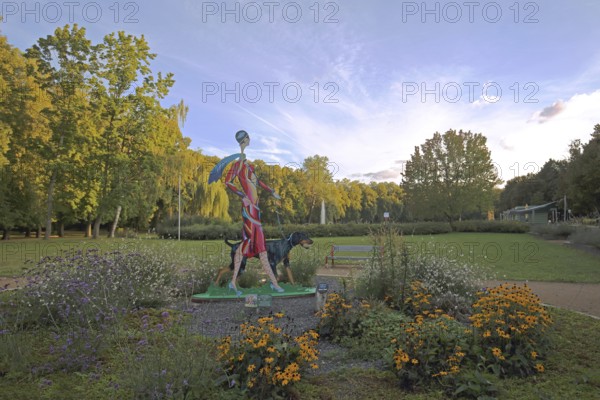Sculpture Lady with Doberman by Carolin Okon 2017, modern art, colourful elegant female figure walking a dog, walk with dog, dog figure, walk, flower bed, sports park, Apolda, Thuringia, Germany