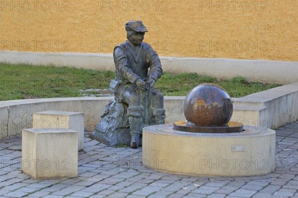 Monument to founder David Strickermann, town history on the development of the textile industry, seated male figure with tub and ball of wool, symbols, wool, ball, bronze sculpture, modern art, rotating granite ball, stone ball, fountain, Strickermannbrunnen, Schulplatz, Apolda, Thuringia, Germany