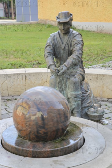 Monument to founder David Strickermann, town history on the development of the textile industry, seated male figure with tub and ball of wool, symbols, wool, ball, bronze sculpture, modern art, rotating granite ball, stone ball, fountain, Strickermannbrunnen, Schulplatz, Apolda, Thuringia, Germany