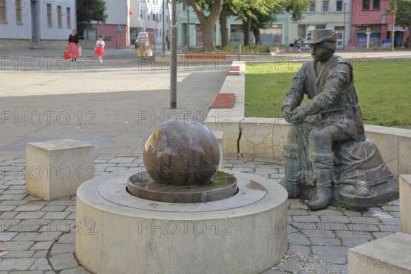 Monument to founder David Strickermann, town history on the development of the textile industry, seated male figure with tub and ball of wool, symbols, wool, ball, bronze sculpture, modern art, rotating granite ball, stone ball, fountain, Strickermannbrunnen, Schulplatz, Apolda, Thuringia, Germany