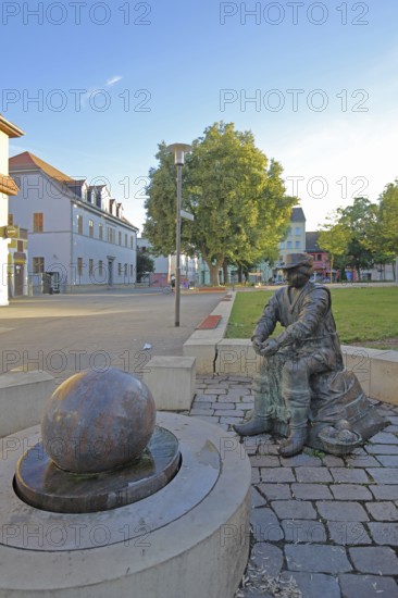 Monument to founder David Strickermann, town history on the development of the textile industry, seated male figure with tub and ball of wool, symbols, wool, ball, bronze sculpture, modern art, rotating granite ball, stone ball, fountain, Strickermannbrunnen, Schulplatz, Apolda, Thuringia, Germany