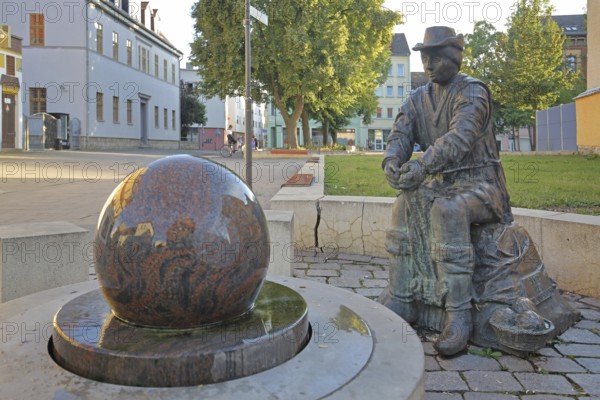 Monument to founder David Strickermann, town history on the development of the textile industry, seated male figure with tub and ball of wool, symbols, wool, ball, bronze sculpture, modern art, rotating granite ball, stone ball, fountain, Strickermannbrunnen, Schulplatz, Apolda, Thuringia, Germany