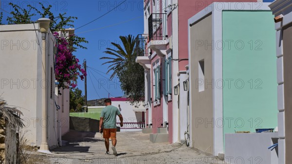 A man walks along a sunny street, past colourfully painted buildings with Mediterranean flair, Kattavia village, southern tip of Rhodes, Rhodes, Dodecanese, Greek Islands, Greece
