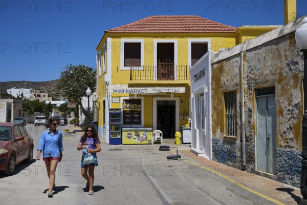 Two woman in summer clothes walking along a yellow building, Kattavia village, southern tip of Rhodes, Rhodes, Dodecanese, Greek Islands, Greece